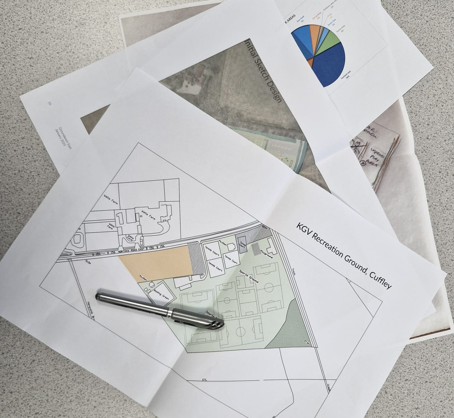 Image shows a pile of four papers, relating to King George V Playing Field, Cuffley, placed on a table with a pen resting on top.